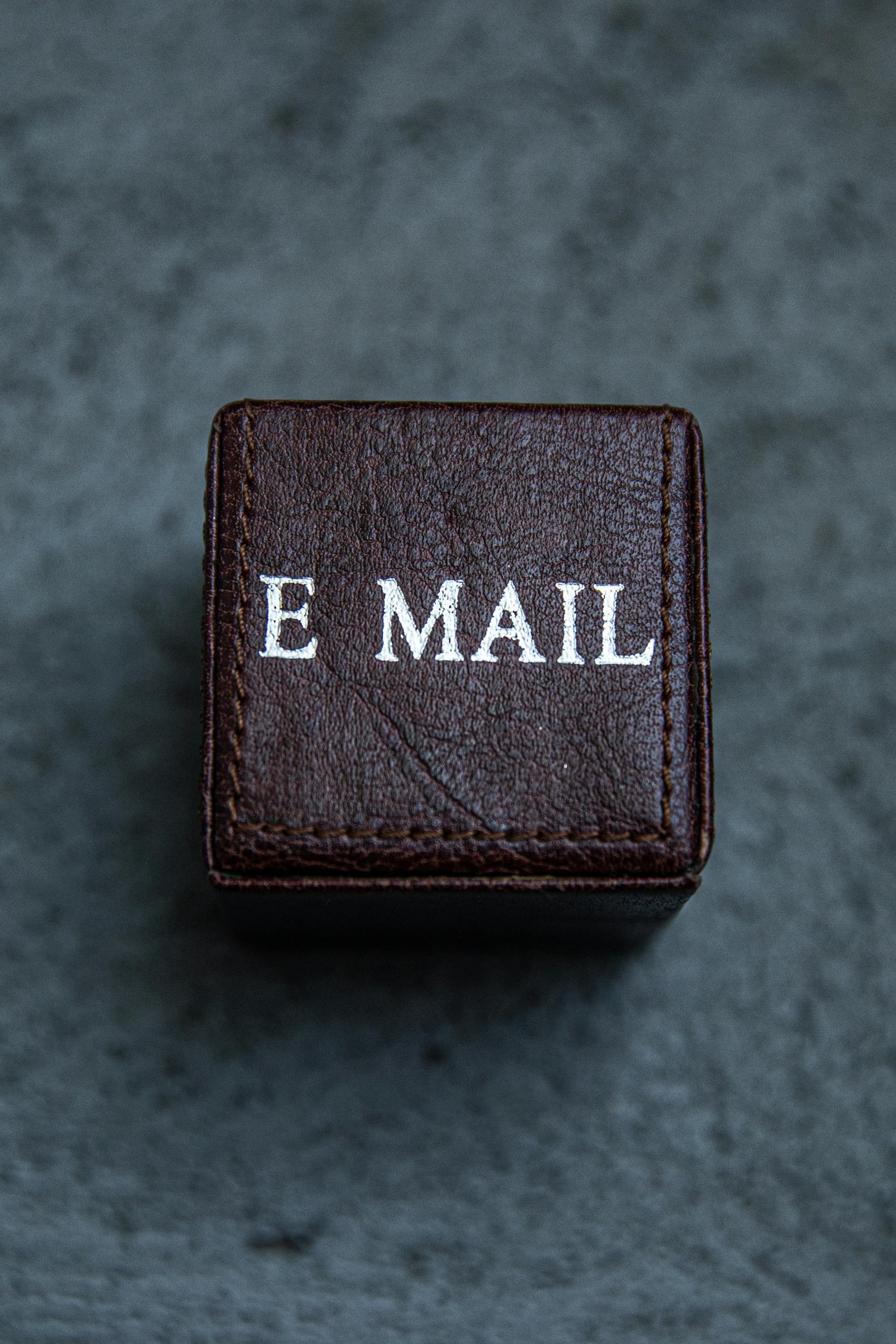 Brown leather square box with 'E MAIL' text on a gray surface, modern still life